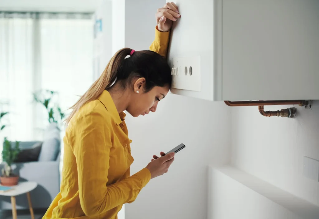 Homeowner checking her phone beside a broken boiler